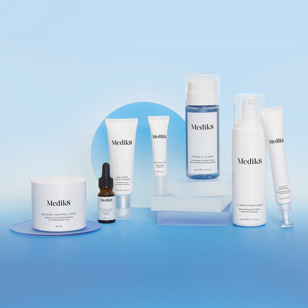 Medik8-produkter för att bekämpa blemmor, inklusive Blemish Control Pads, Press & Clear och Clarifying Foam, arrangerade på en blå bakgrund.