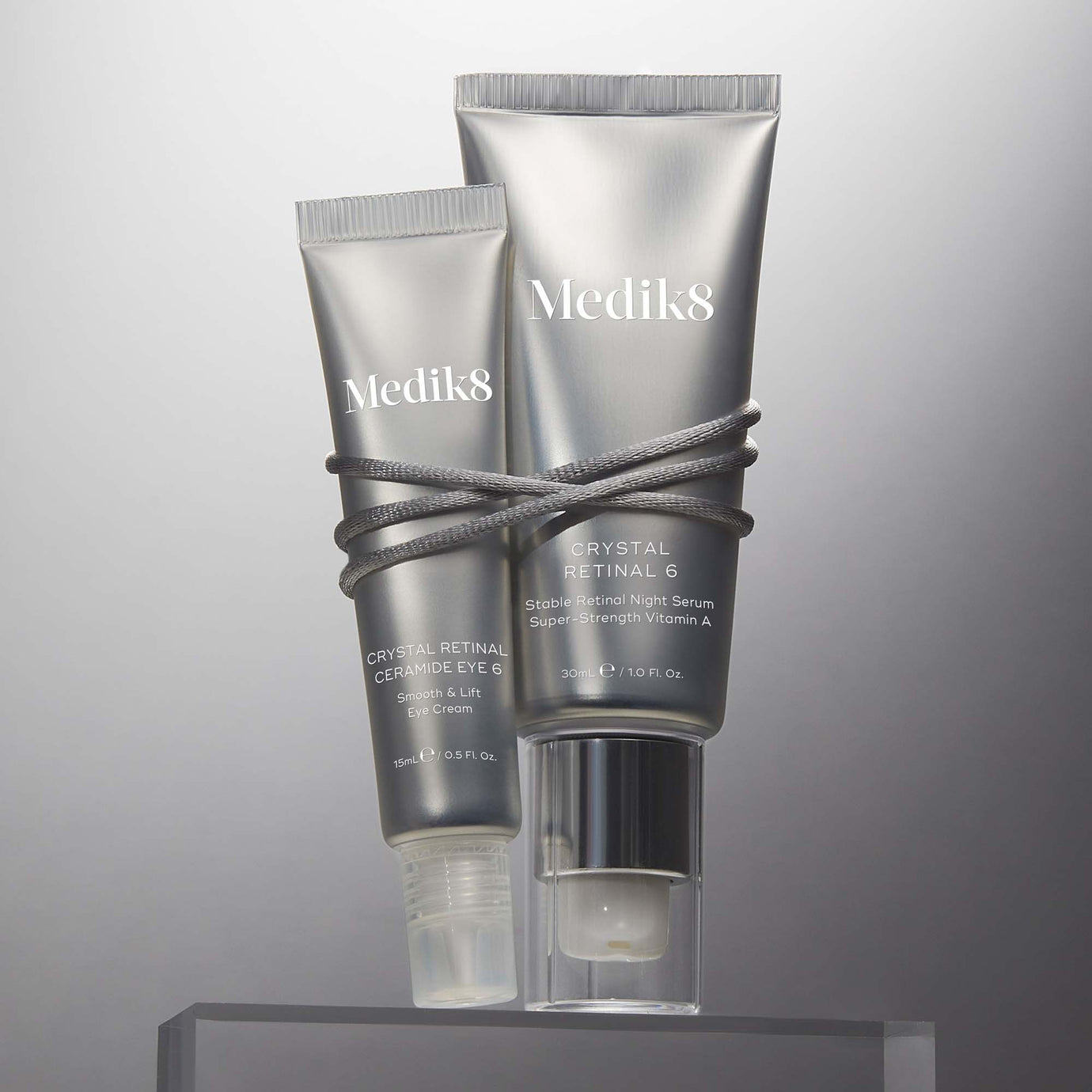 Crystal Retinal 6 och Ceramide Eye 6 ögonkräm bundna med en silvertråd, presenterade på en genomskinlig yta. Crystal Retinal 6 och Ceramide Eye 6 ögonkräm bundna med en silvertråd, presenterade på en genomskinlig yta.