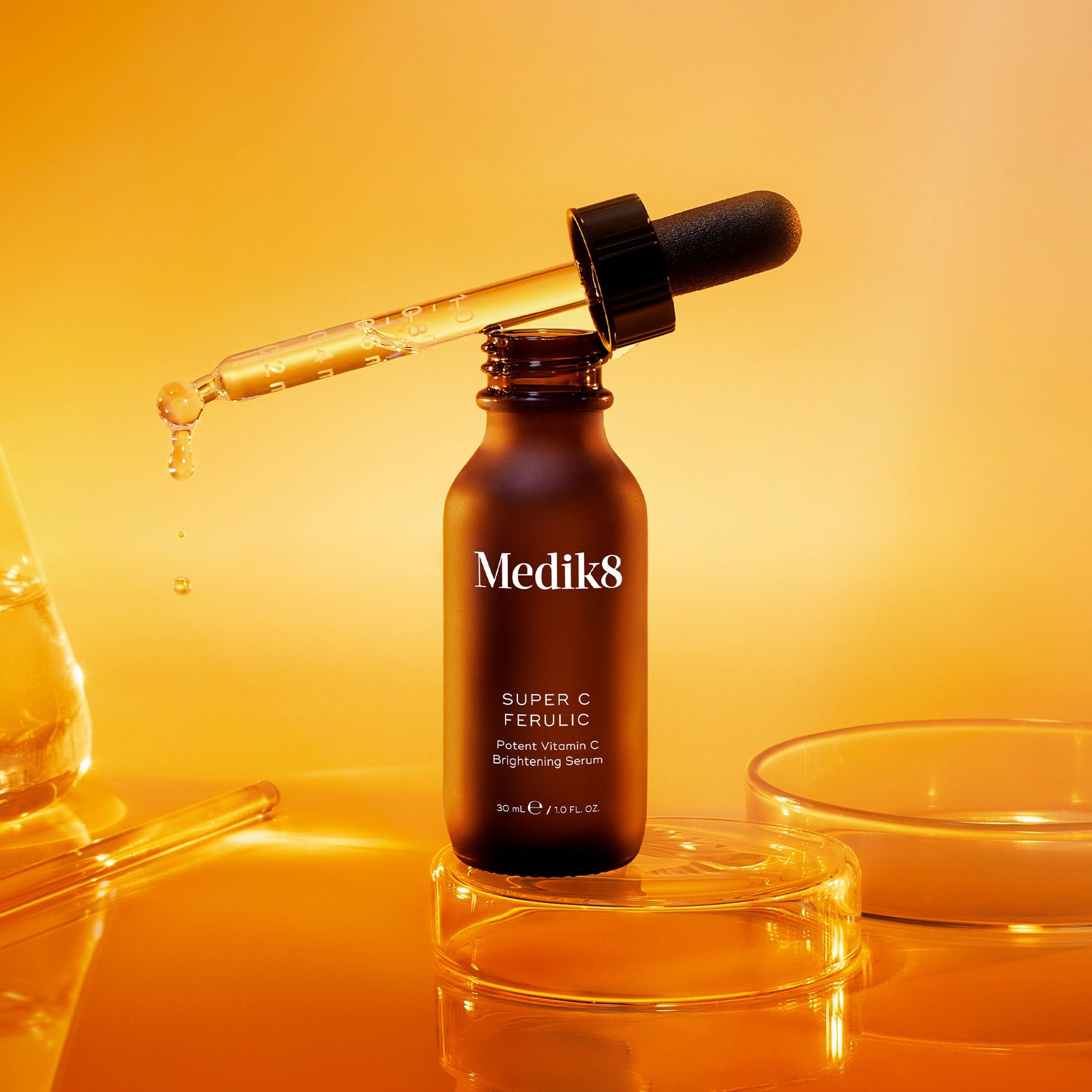 Super C Ferulic-serum med en pipett som släpper droppar, fotograferat mot en varm, gyllene bakgrund.
