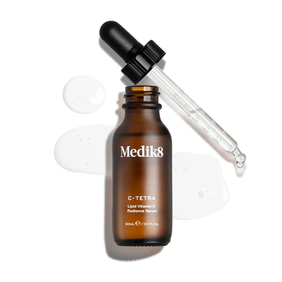 Medik8 C-Tetra Vitamin C-serum i brun glasflaska med pipett, omgiven av genomskinliga droppar serum.-2