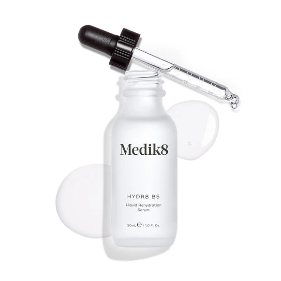 Produktbild av Medik8 Hydr8 B5, ett återfuktande serum i en vit glasflaska med pipett, tillsammans med droppar av serumet i bakgrunden-9