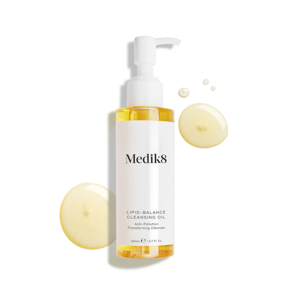 Produktbild av Medik8 Lipid-Balance Cleansing Oil, en rengöringsolja i en genomskinlig pumpflaska, tillsammans med ljusgula droppar i bakgrunden.