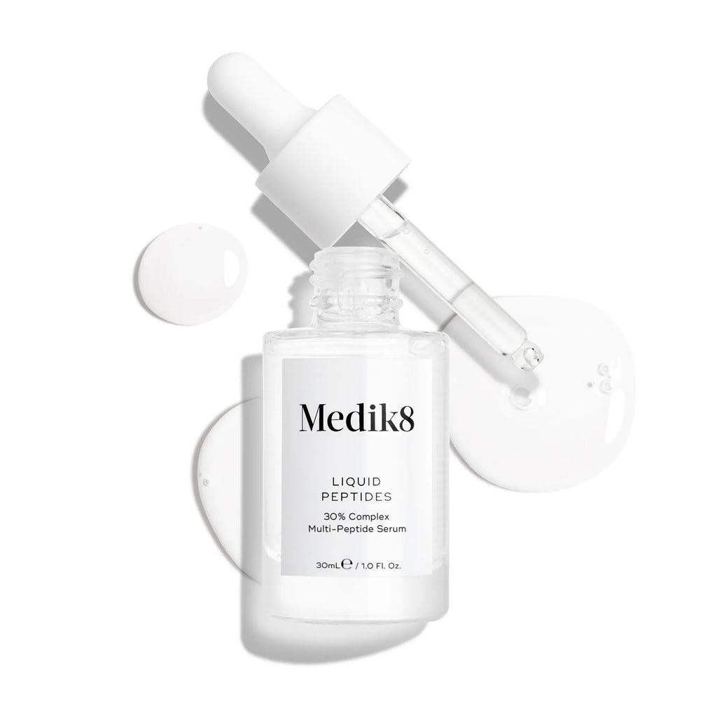 Produktbild av Medik8 Liquid Peptides, ett serum i en genomskinlig glasflaska med en pipett, tillsammans med vita droppar i bakgrunden.