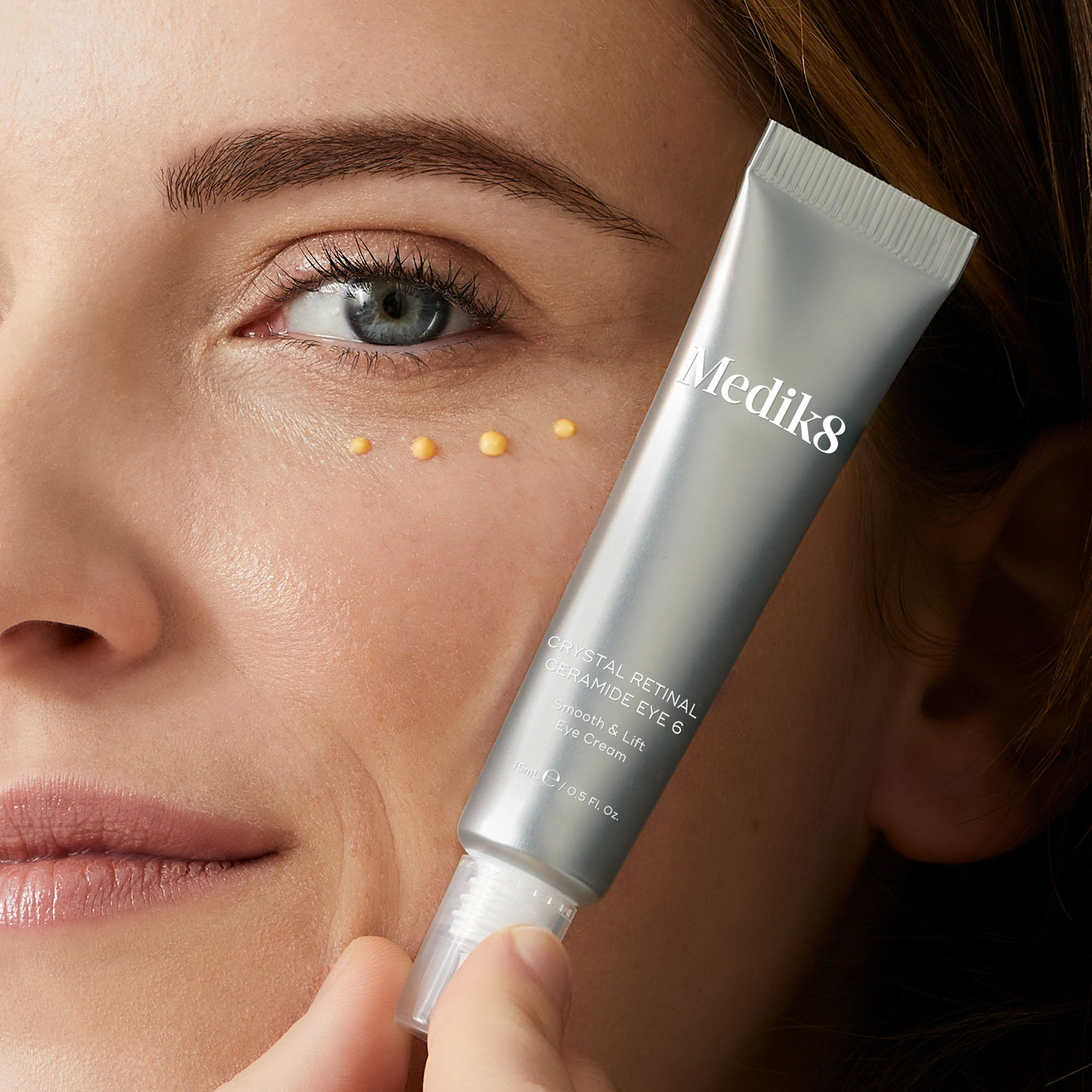 Närbild av en kvinna som applicerar Medik8 Crystal Retinal Ceramide Eye-kräm under ögonen, med produkten i förgrunden