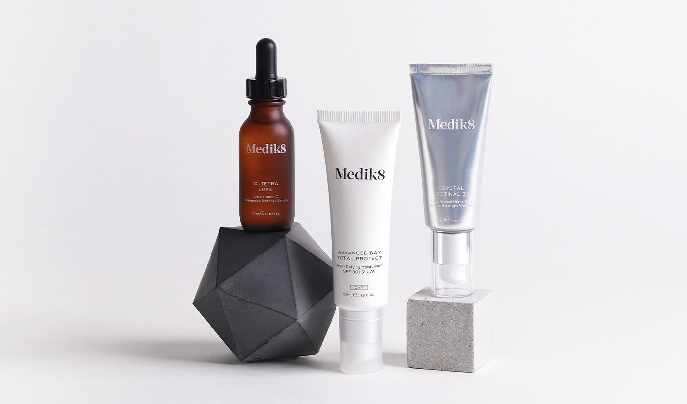 Tre Medik8-produkter: C-Tetra Luxe serum, Advanced Day Total Protect SPF 30 och Crystal Retinal 3, stylade på geometriska block.