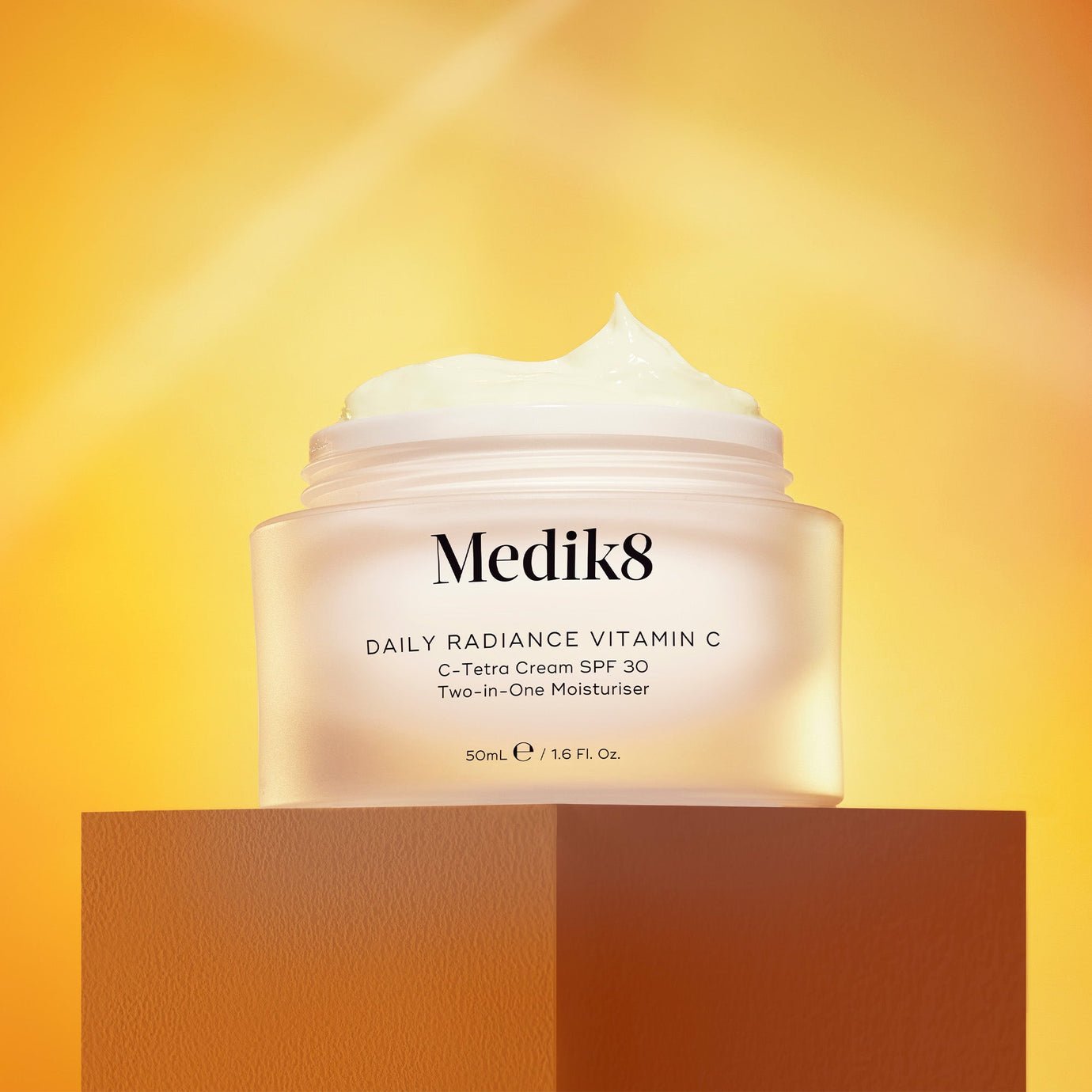 Daily Radiance Vitamin C-kräm med SPF 30 placerad på en orange piedestal, upplyst av mjuka solnedgångstoner.