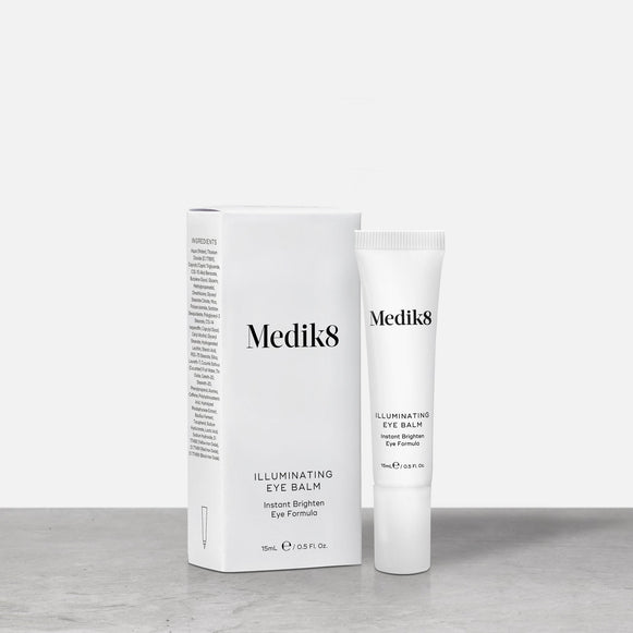 Produktbild av Medik8 Illuminating Eye Balm, ett ljusreflekterande ögonbalsam i en vit tub, stående bredvid produktens förpackning.-6