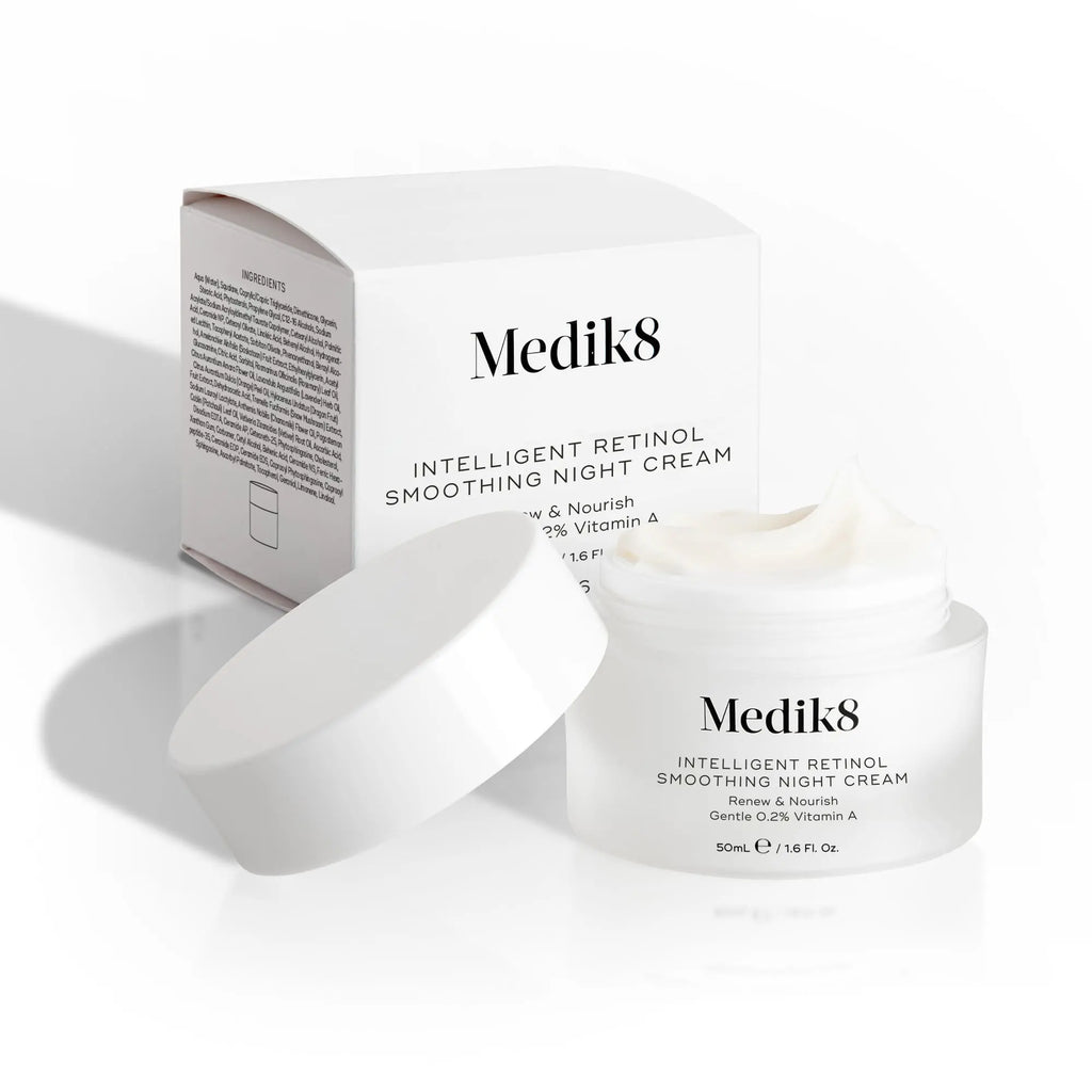 Medik8 Intelligent Retinol Smoothing Night Cream i en vit burk med avtagbart lock, placerad bredvid sin förpackning med minimalistisk design och svart text. Krämen har en fyllig konsistens.